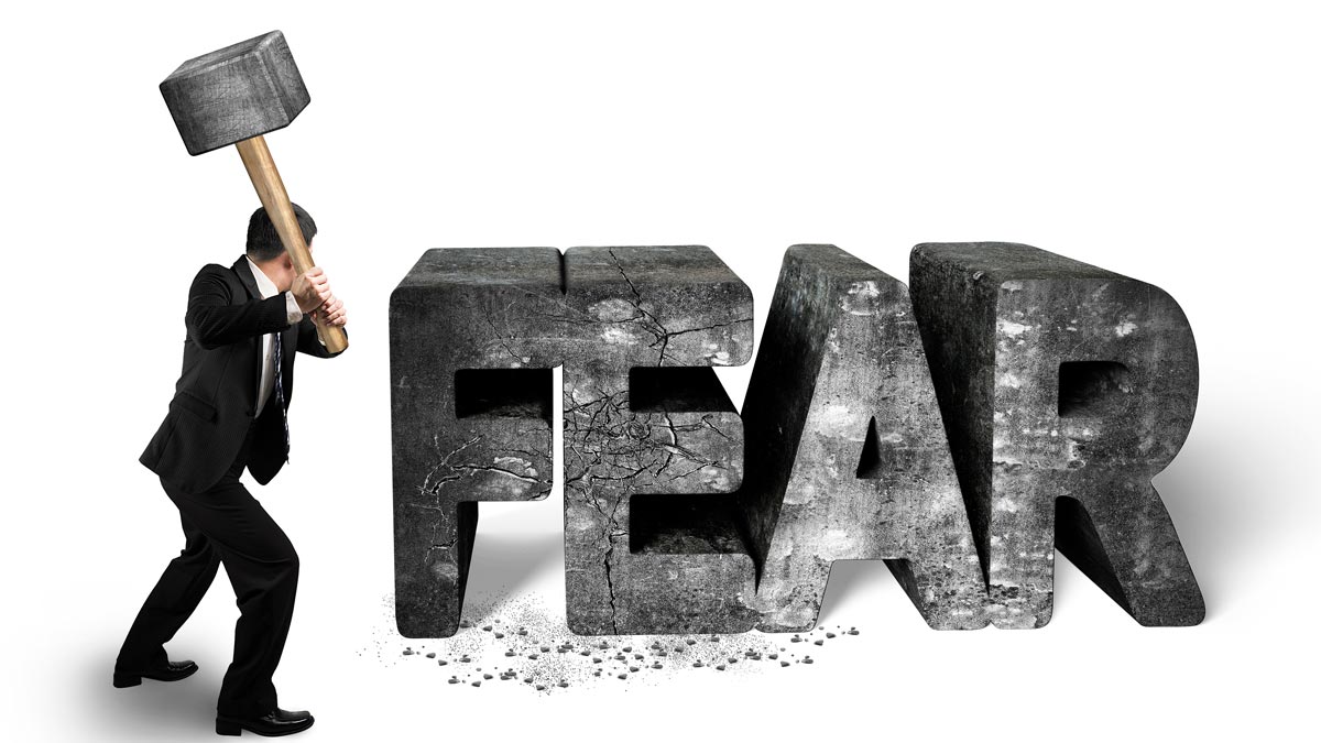 businessman smashing the word fear with a large hammer overcoming fear and limiting beliefs